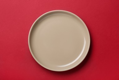 Empty beige ceramic plate on red background, top view