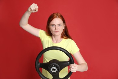 Emotional young woman with steering wheel on red background