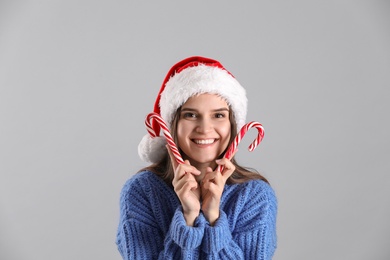 Pretty woman in Santa hat and blue sweater holding candy canes on grey background