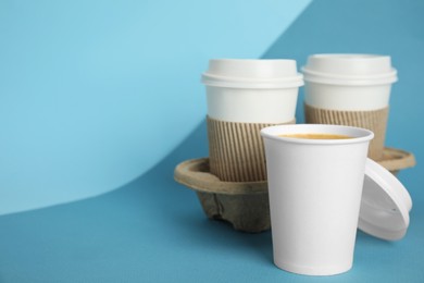 Takeaway paper coffee cups with sleeves, plastic lids and cardboard holder on blue background, space for text