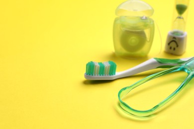 Tongue cleaner, toothbrush, dental floss and hourglass on yellow background, closeup. Space for text