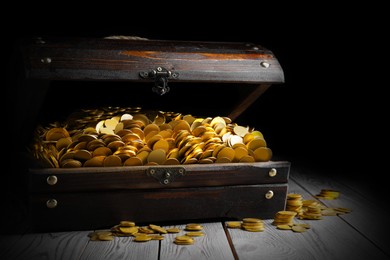 Open treasure chest with gold coins on grey wooden table