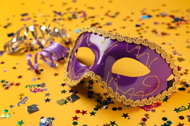 Beautiful purple carnival mask and confetti on yellow background, closeup