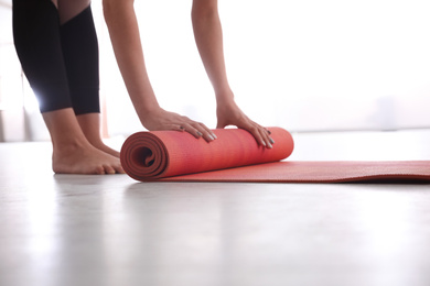 Woman rolling her mat on floor in yoga studio, closeup
