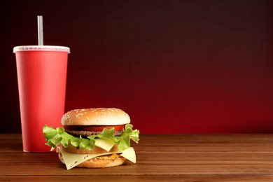 Delicious burger and drink on wooden table against red background, space for text. Fast food menu