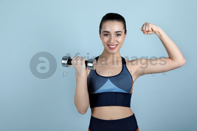 Photo of Woman with dumbbell as girl power symbol on light grey background. 8 March concept