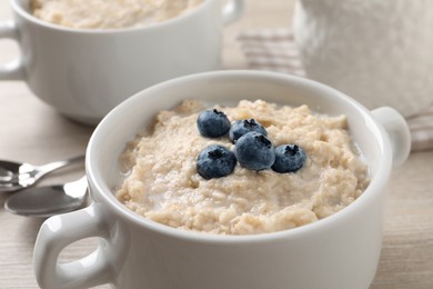 Tasty oatmeal porridge with blueberries in bowl on light table, closeup