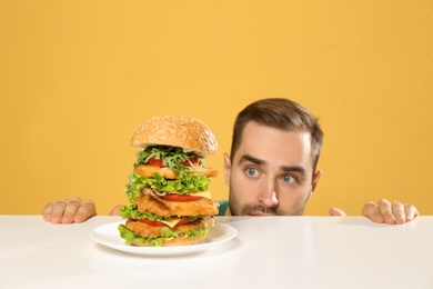 Photo of Young hungry man and huge burger on color background