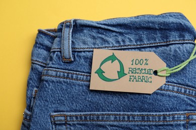 Jeans with recycling label on yellow background, closeup