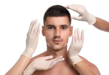 Doctors examining man's face for cosmetic surgery on white background