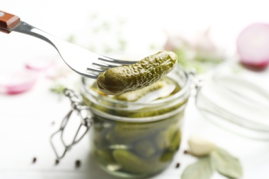 Fork with tasty pickled cucumber near glass jar, closeup