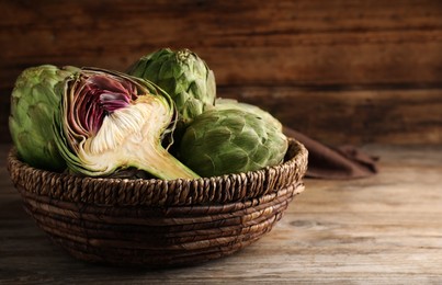 Cut and whole fresh raw artichokes in basket on wooden table