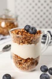 Tasty yogurt with muesli and blueberries in cup served on white wooden table