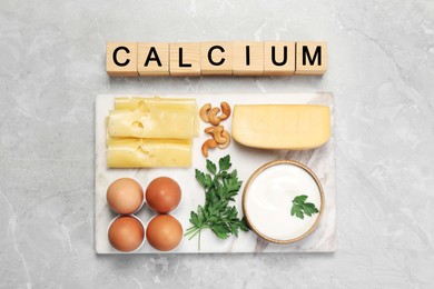 Photo of Set of natural food and cubes with word Calcium on grey marble table, flat lay