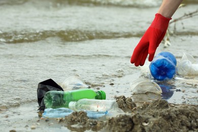 Woman in gloves collecting garbage on beach, closeup