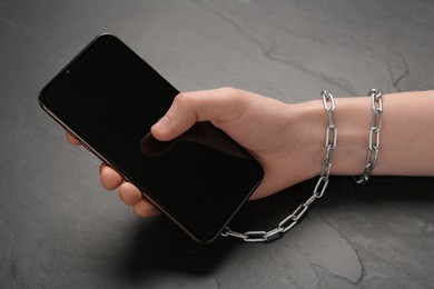 Internet addiction. Top view of man holding phone at wooden table, hand tied to device with chain