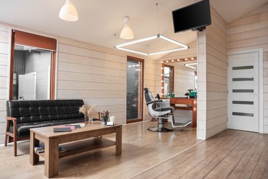 Photo of Stylish barbershop interior with hairdresser's workplace, leather sofa and wooden coffee table
