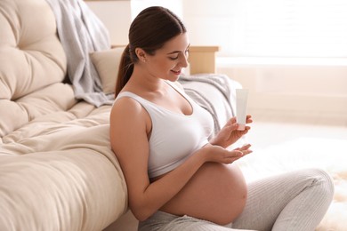 Young pregnant woman with cosmetic product at home