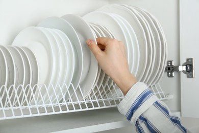 Photo of Woman taking ceramic plate from drying rack, closeup