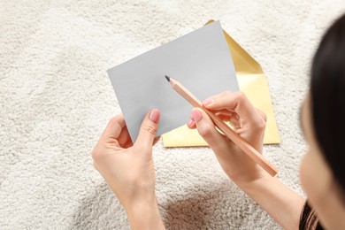 Woman writing message in greeting card on carpet in room, closeup