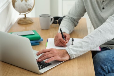 Man with laptop and notebook learning at wooden table indoors, closeup