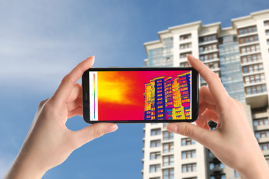 Woman detecting heat loss in building using thermal viewer on smartphone, outdoors. Energy efficiency