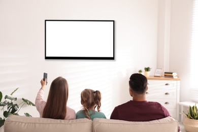 Photo of Family watching TV on sofa at home, back view