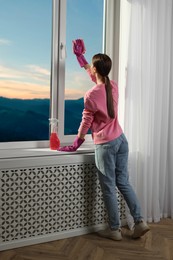Young woman cleaning window glass with rag at home, back view