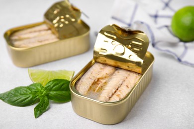 Photo of Open tin cans with mackerel fillets, lime and basil on grey table