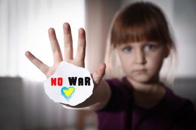 Unhappy little girl showing palm with phrase No War at home, focus on hand