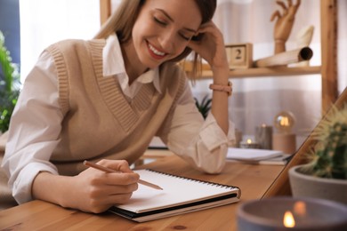 Young woman drawing in sketchbook with pencil at wooden table indoors, focus on hand