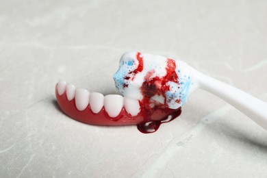 Gum model and toothbrush with blood on light grey table, closeup