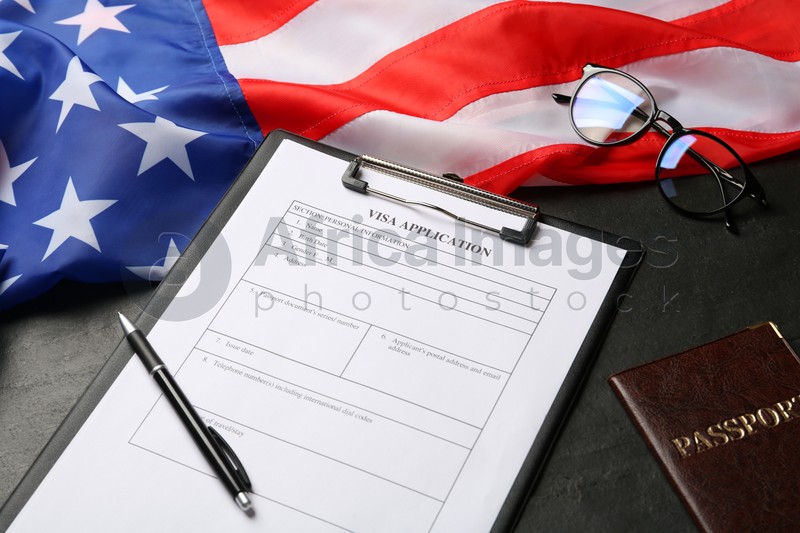 Photo of American flag, visa application form, passport and glasses on black table