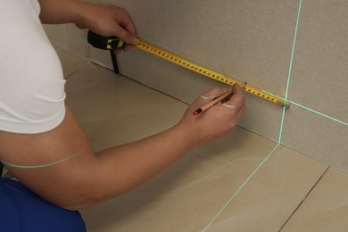 Worker using cross line laser level, pencil and tape for accurate measurement on plasterboard, closeup