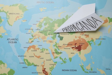 Photo of Paper airplane with word Propaganda on world map, top view. Information warfare concept