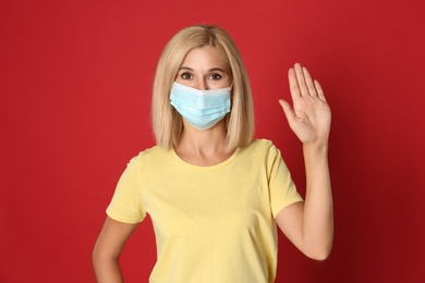Woman in protective mask showing hello gesture on red background. Keeping social distance during coronavirus pandemic