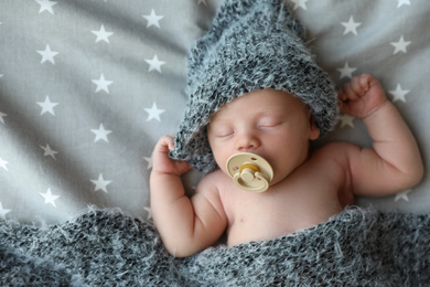 Cute newborn baby in warm hat sleeping on bed, top view