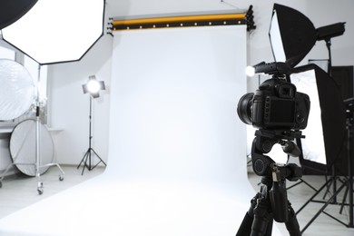 Photo of Tripod with camera and professional lighting equipment in modern photo studio. Space for text