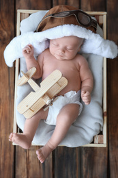 Cute newborn baby wearing aviator hat in wooden crate, top view