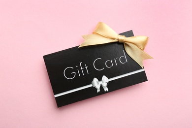 Gift card with bow on pink background, top view