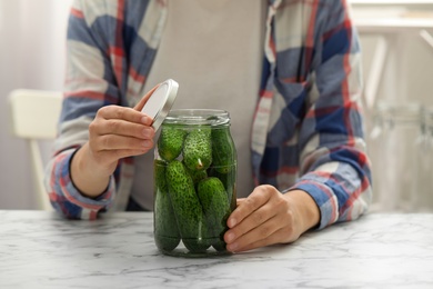 Woman pickling glass jar of cucumbers at white marble kitchen table, closeup
