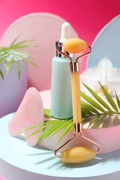 Beautiful composition with gua sha stone, face roller and bottle of serum on pink background