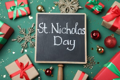 Small chalkboard with text St. Nicholas Day, gift boxes and festive decor on green background, flat lay