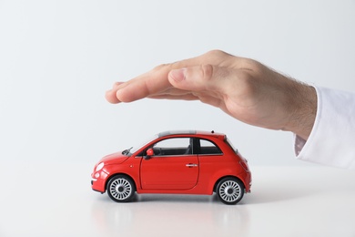 Male insurance agent covering toy car on white background, closeup