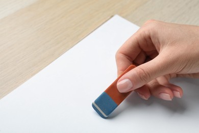 Woman erasing something in notebook at wooden table, closeup