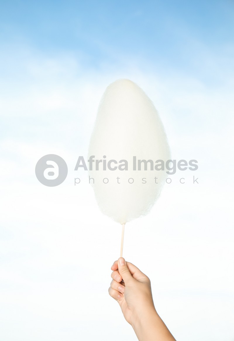 Woman holding sweet cotton candy on blue sky background, closeup view