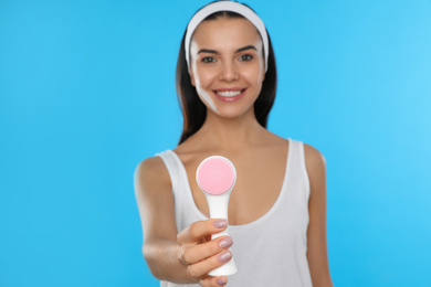 Young woman holding facial cleansing brush on light blue background. Washing accessory