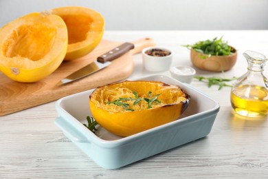 Half of cooked spaghetti squash with arugula in baking dish on white wooden table