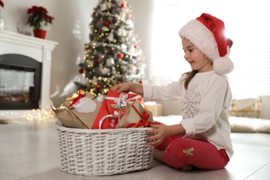 Cute little girl in Santa hat taking gift from Christmas advent calendar at home