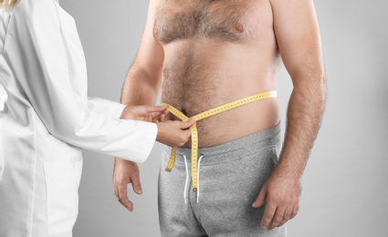 Doctor measuring man's waist on grey background, closeup. Weight loss